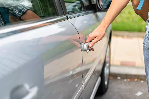 Person attempting to unlock a car with a tool, representing a car lockout service